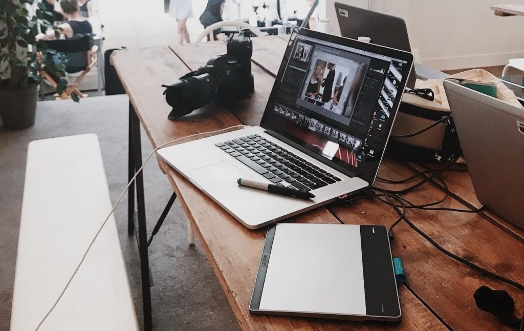 Un espacio de trabajo productivo con herramientas esenciales para el diseño gráfico, como una cámara, un portátil con un programa de edición activo y un bloc de diseño conectado